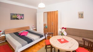 Ein modernes Schlafzimmer mit einem Bett, einem Holzschrank, einem runden Holztisch mit Stühlen und einem Sofa.