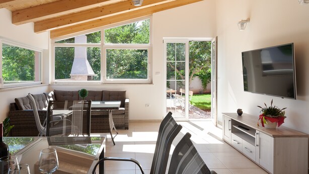 A modern living room with a dining area, large windows, a TV, and a sliding glass door leading to a patio. - Holiday Home Hana (Medulin)