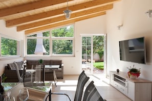 A modern living room with a dining area, large windows, a TV, and a sliding glass door leading to a patio. - Holiday Home Hana (Medulin)
