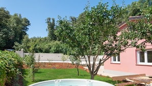 A hot tub in a backyard with a pink house, a tree, and a wooden bench. - Holiday Home Hana (Medulin)
