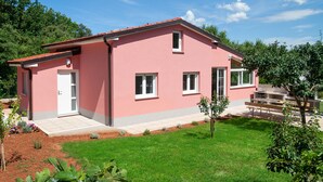 A pink building with a red roof, a white door, and a small garden with a bench. - Holiday Home Hana (Medulin)