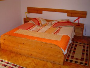 A wooden bed with a striped bedspread and pillows, a nightstand with a lamp, and a patterned rug on a wooden floor.