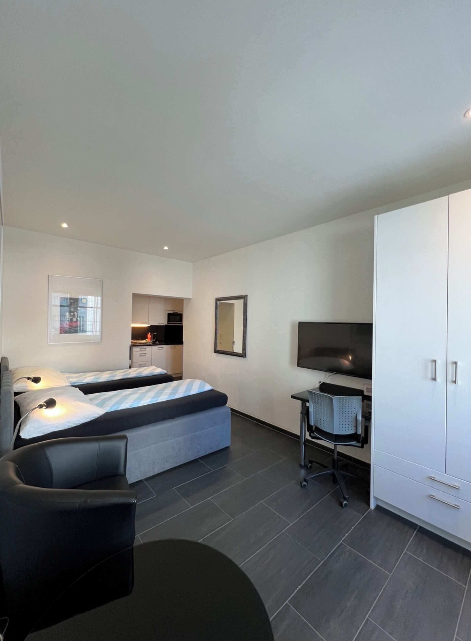 A modern hotel room with two beds, a desk, a TV, and a wardrobe.