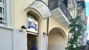 A building entrance with a gated driveway, a small landscaped area with a tree, and a sign for a hotel or apartment complex.