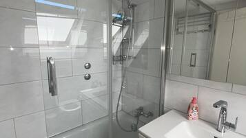 Un baño moderno con ducha envuelta en vidrio, lavabo blanco y un espejo grande.