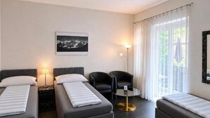 A modern hotel room with two single beds, a small round table, a chair, a floor lamp, and a large window with curtains.