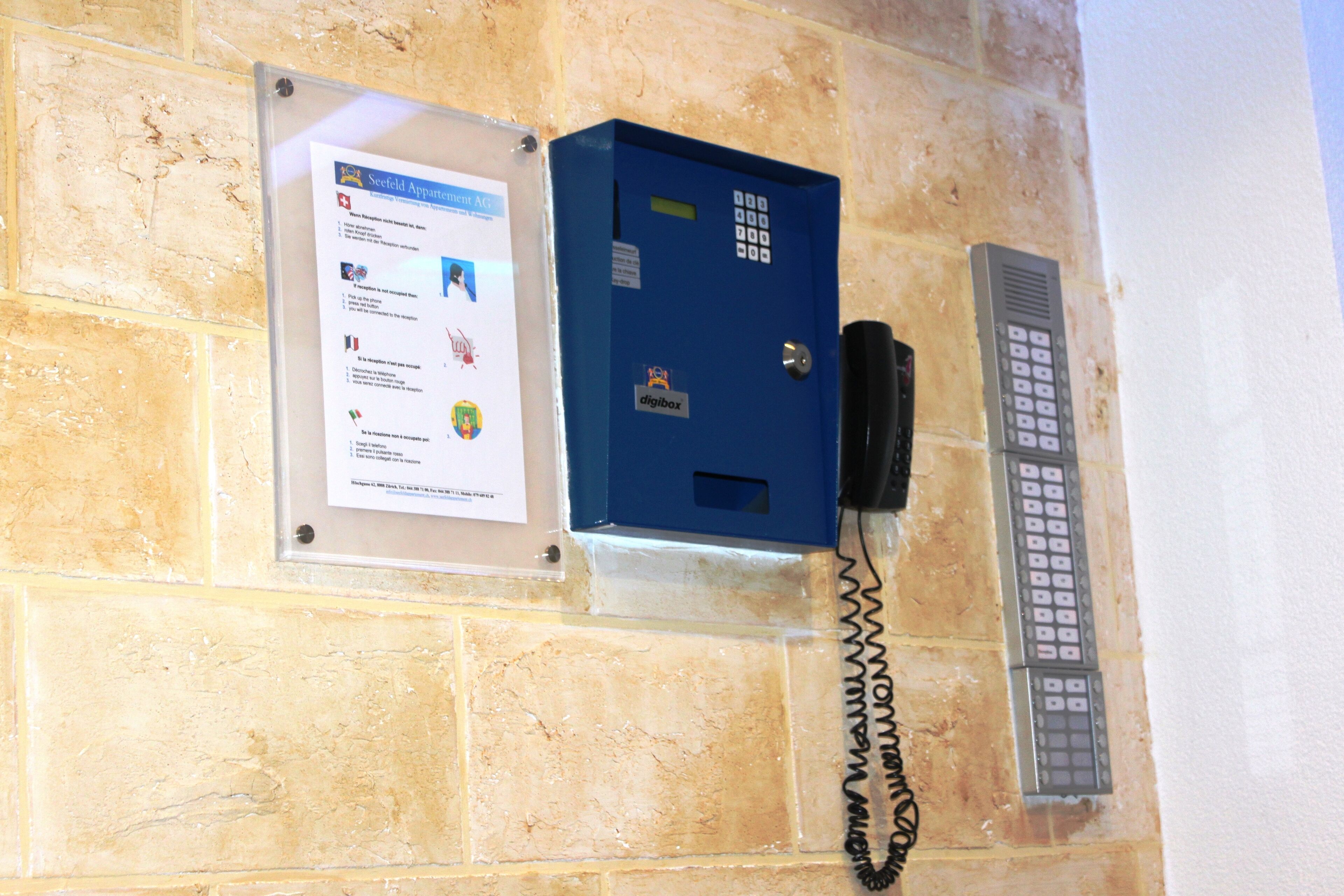 A blue security box with a keypad and a telephone on a beige wall.