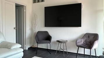 A modern living room with a white sofa, two armchairs, a coffee table, and a flat-screen TV mounted on the wall.