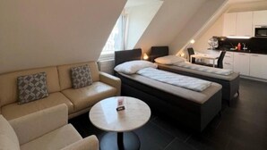 A modern loft bedroom with a sofa, a bed, a small table, and a kitchenette.