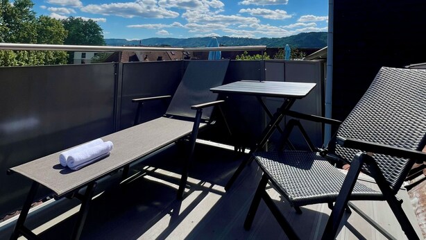 A rooftop terrace with a table and chairs, a view of the sky, and a distant landscape.