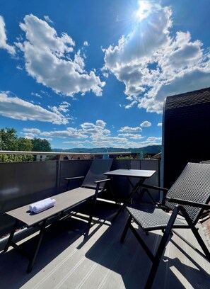 A rooftop terrace with a table and chairs, a view of the sky, and a distant landscape. - Seefeld Residenz GmbH (Zürich)