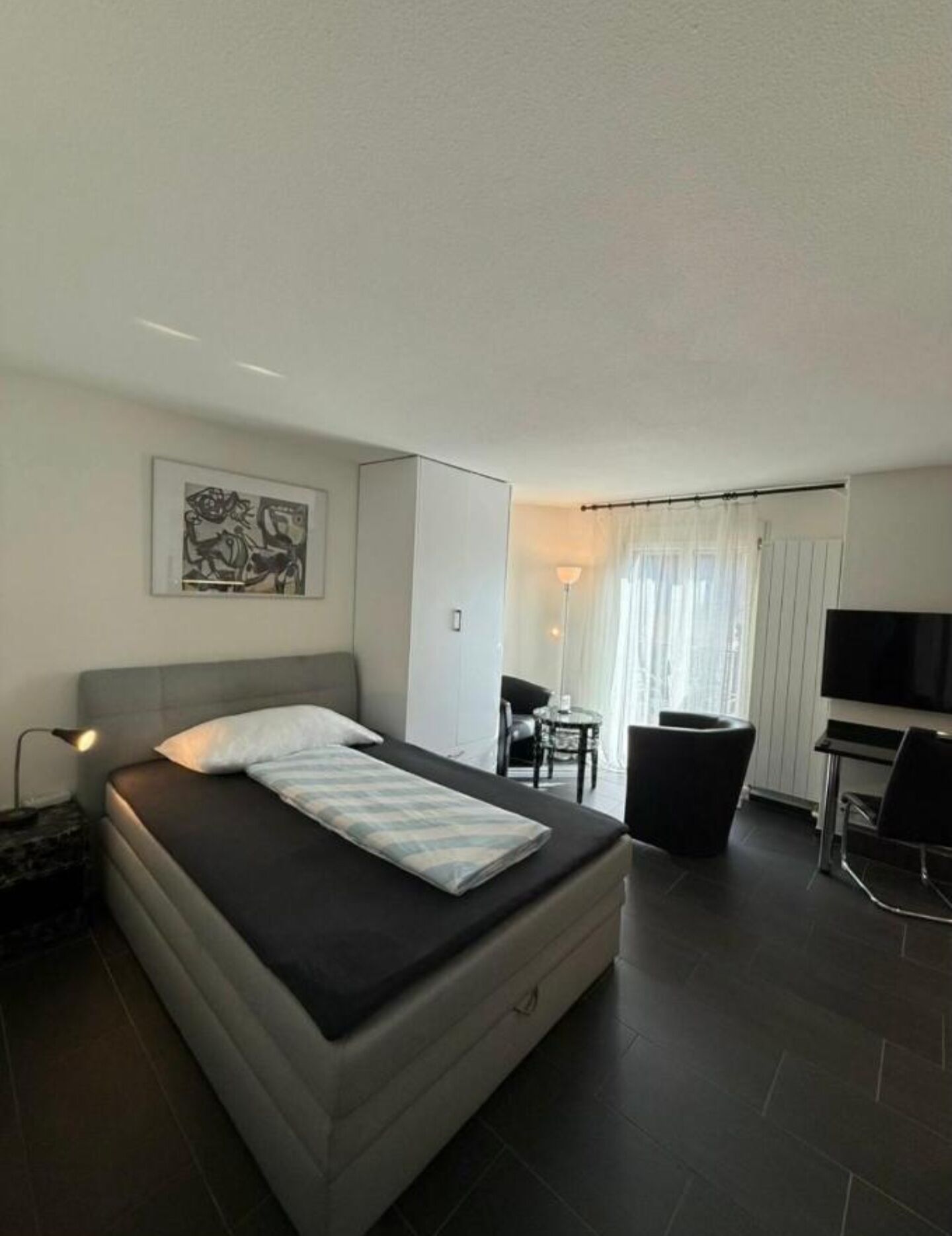 A modern hotel room with a bed, a desk, a chair, and a TV.