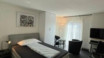 A modern hotel room with a bed, a desk, a chair, and a TV.