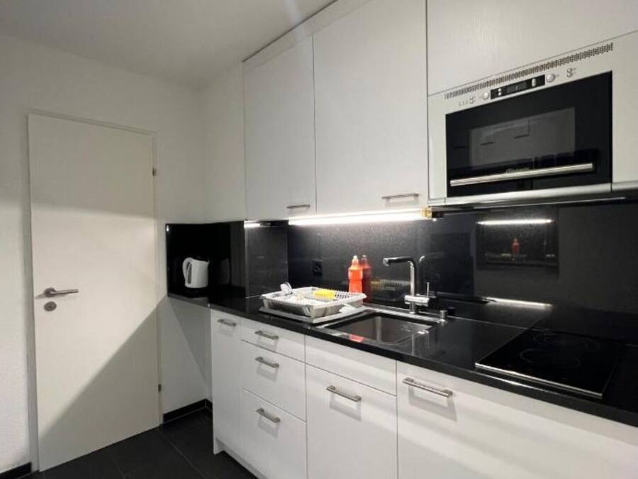 A modern kitchen with white cabinets, a black countertop, a built-in oven, and a stainless steel sink.