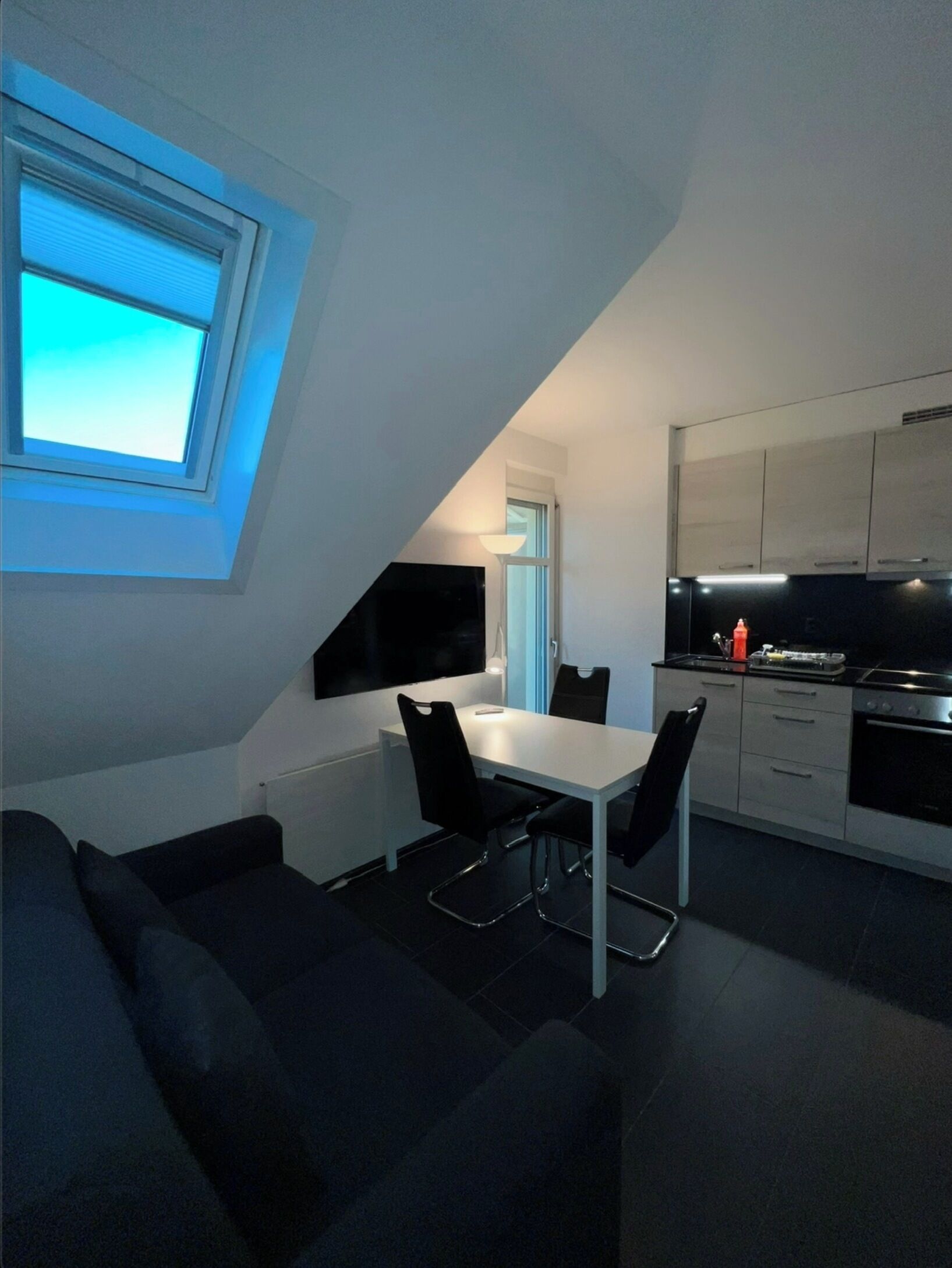 Eine moderne Küche mit Essbereich, einem an der Wand montierten Fernseher und einem Fenster mit Jalousien.