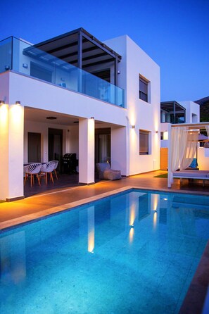 Una casa moderna de dos pisos con piscina, mobiliario de exterior y cama con dosel.