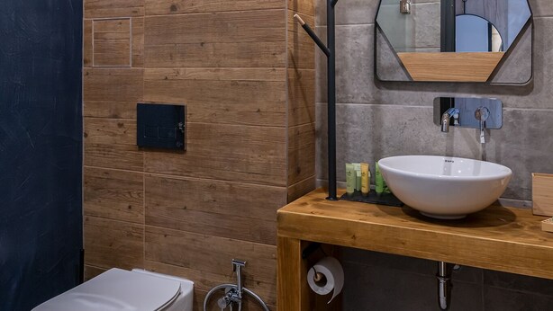 Un bany modern amb un penjallera de fusta, un lavabo blanc, un mirall i un vàter.