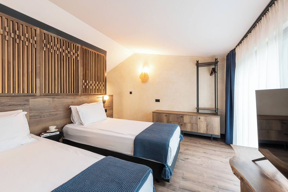 Une chambre d’hôtel avec deux lits, une tête de lit en bois, une table de chevet avec une lampe, une armoire et un grand miroir.
