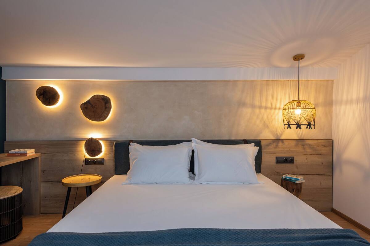 Une chambre à coucher moderne avec un grand lit, une tête de lit en bois et un luminaire mural original.
