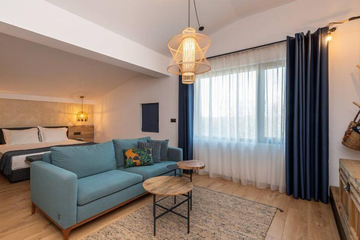 Une chambre moderne avec un lit, un canapé bleu, une petite table ronde et un luminaire suspendu.