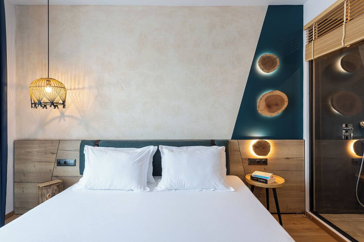 Une chambre d’hôtel moderne avec un grand lit, une table de chevet sur laquelle repose un livre, et un décor mural original composé de motifs circulaires.
