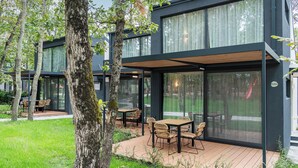Un edificio moderno con amplios ventanales y una terraza de madera con asientos exteriores.