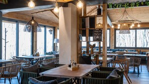 Un restaurante con mesas y sillas de madera, luces colgantes y un techo con follaje verde.