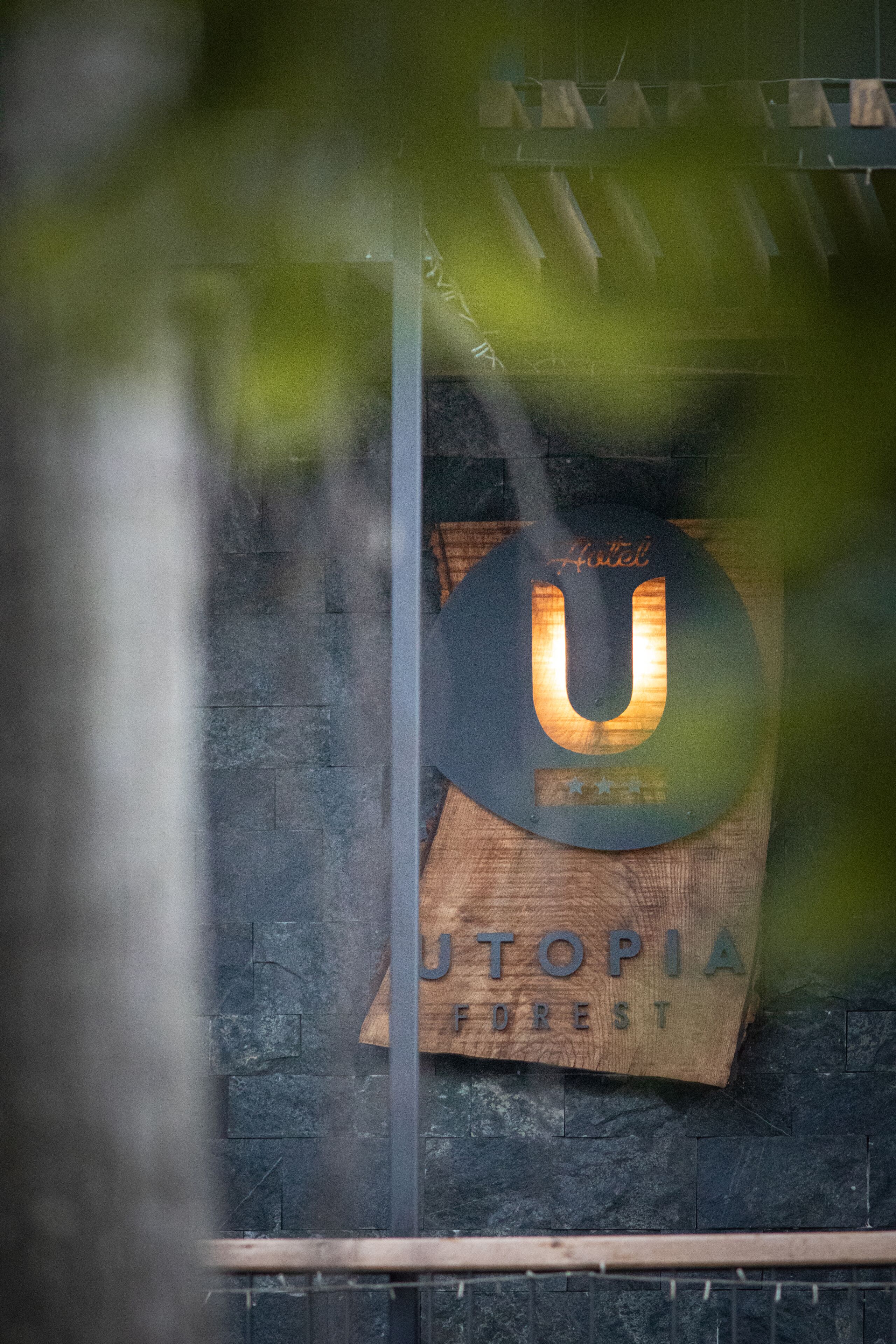 Ein Hotelschild mit dem Namen "UTOPIA FOREST" und einem großen, beleuchteten 'U' auf einer Holztafel.
