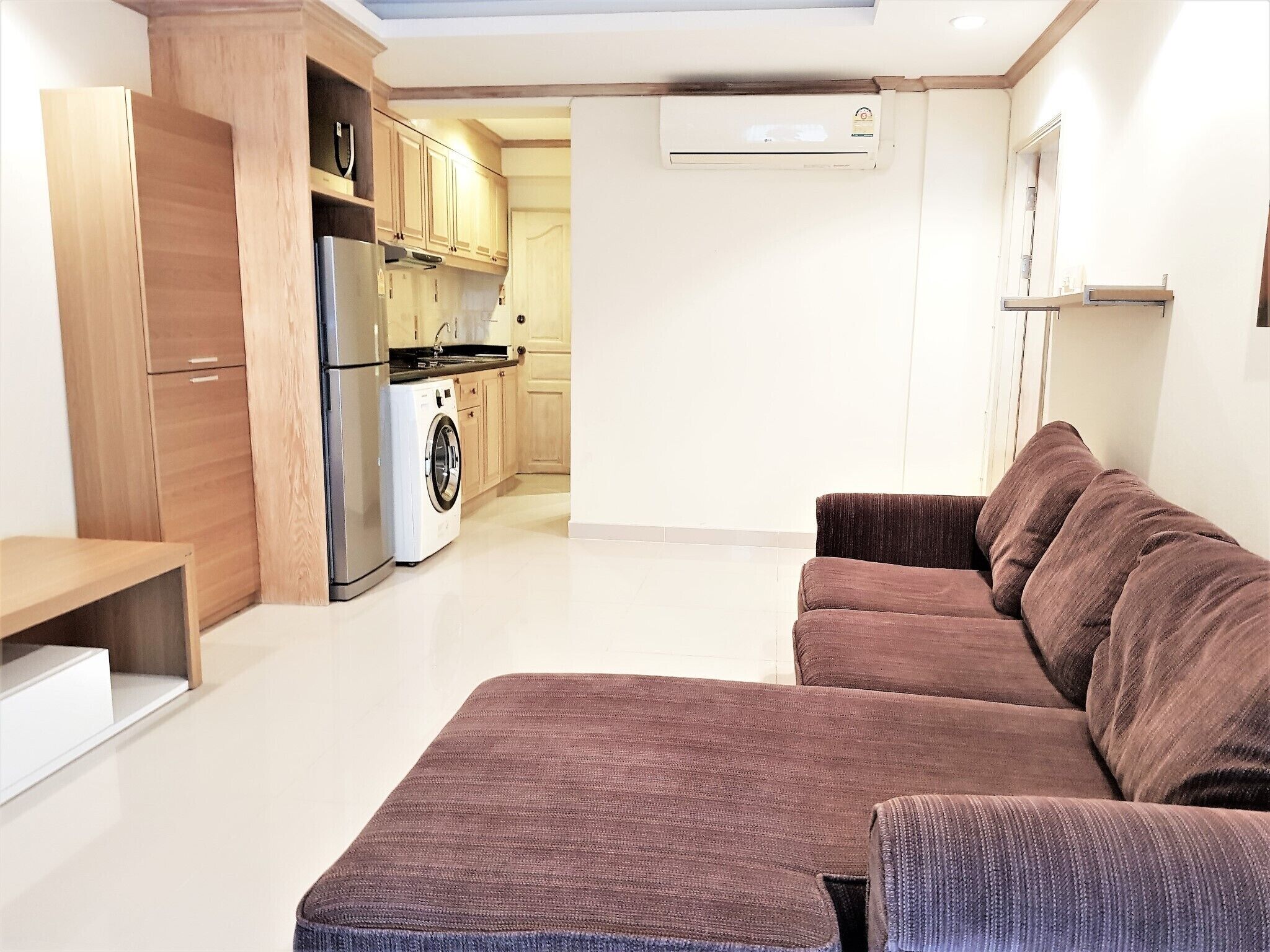 Un espace de vie compact comprenant un coin cuisine, un lave-linge et un canapé marron.