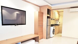 Een moderne woonkamer met een flatscreen televisie, een houten bank en een wasmachine op de achtergrond.