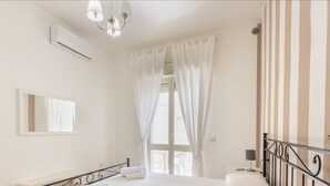A hotel room with a bed, a bedside table, a mirror, a window with curtains, a chandelier, and a striped wall. - Anita Apartment (Noto)