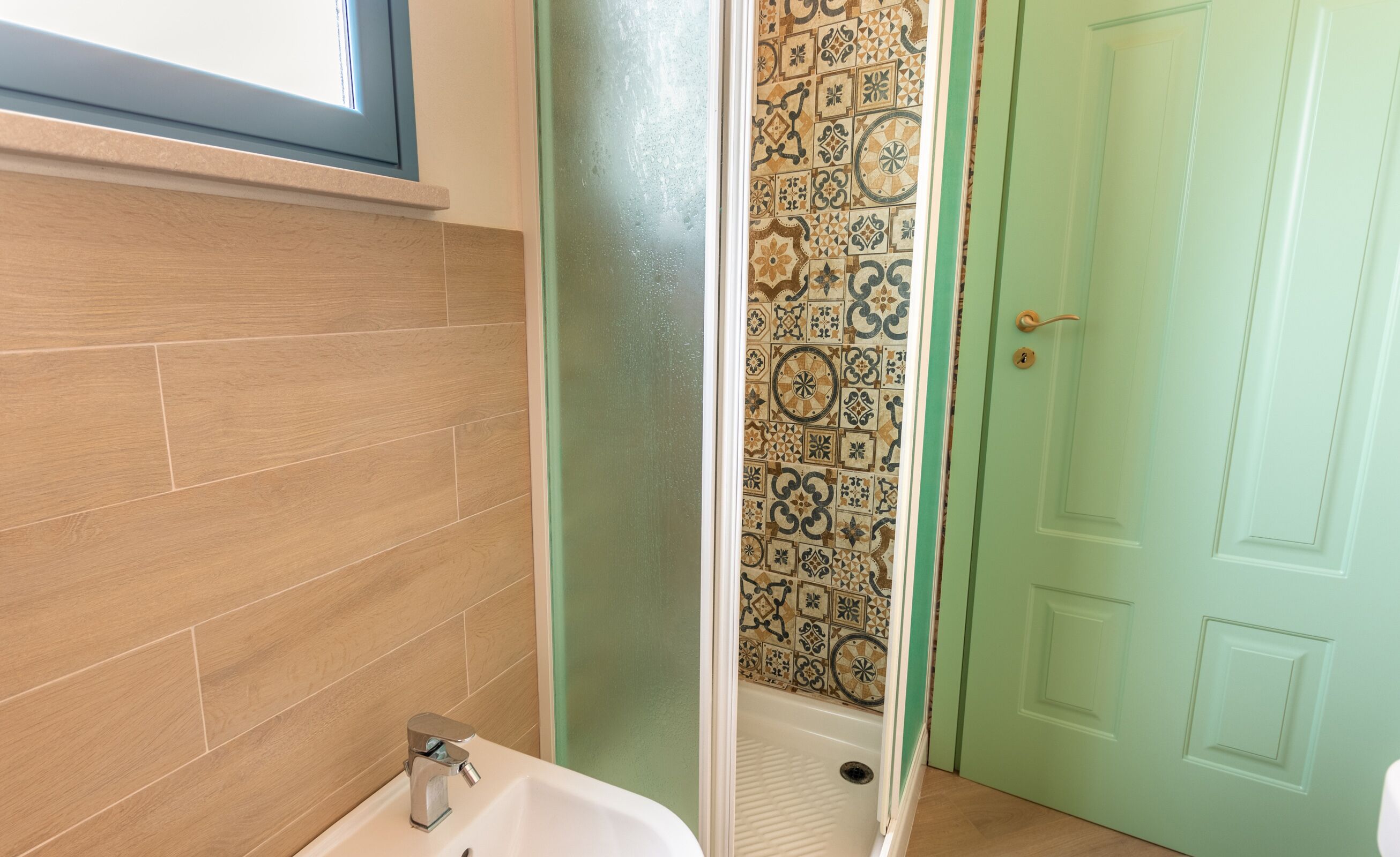 Un baño con suelo de madera, un lavamanos blanco y una puerta verde.