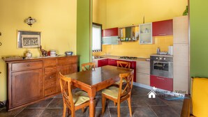 A compact kitchen with a wooden table and chairs, a built-in oven, and a small refrigerator. - Garden Chich (Noto)