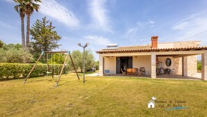 A house with a patio, outdoor seating, and a swing set in a grassy area. - Garden Chich (Noto)