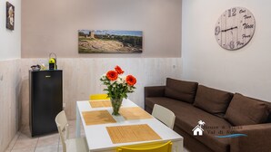 A dining area with a table, chairs, a vase with flowers, a clock, and a refrigerator.