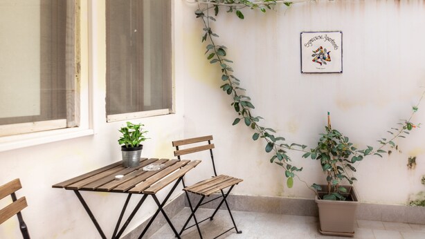 A small patio with a wooden table and chairs, a potted plant, and a wall-mounted sign.