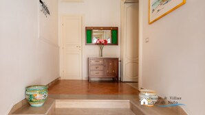 A hallway with a wooden floor, a white door, a mirror with a green frame, a wooden cabinet, and a framed picture on the wall. - Liberty Guest House (Avola)