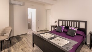 A bedroom with a bed, a chair, a nightstand, and an air conditioning unit.