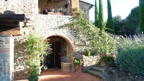 A stone building with an arched entrance, a balcony with flowers, and a garden with lavender.