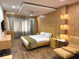 Una habitación de hotel con cama, mesitas de noche, escritorio, silla, televisor y cortina.