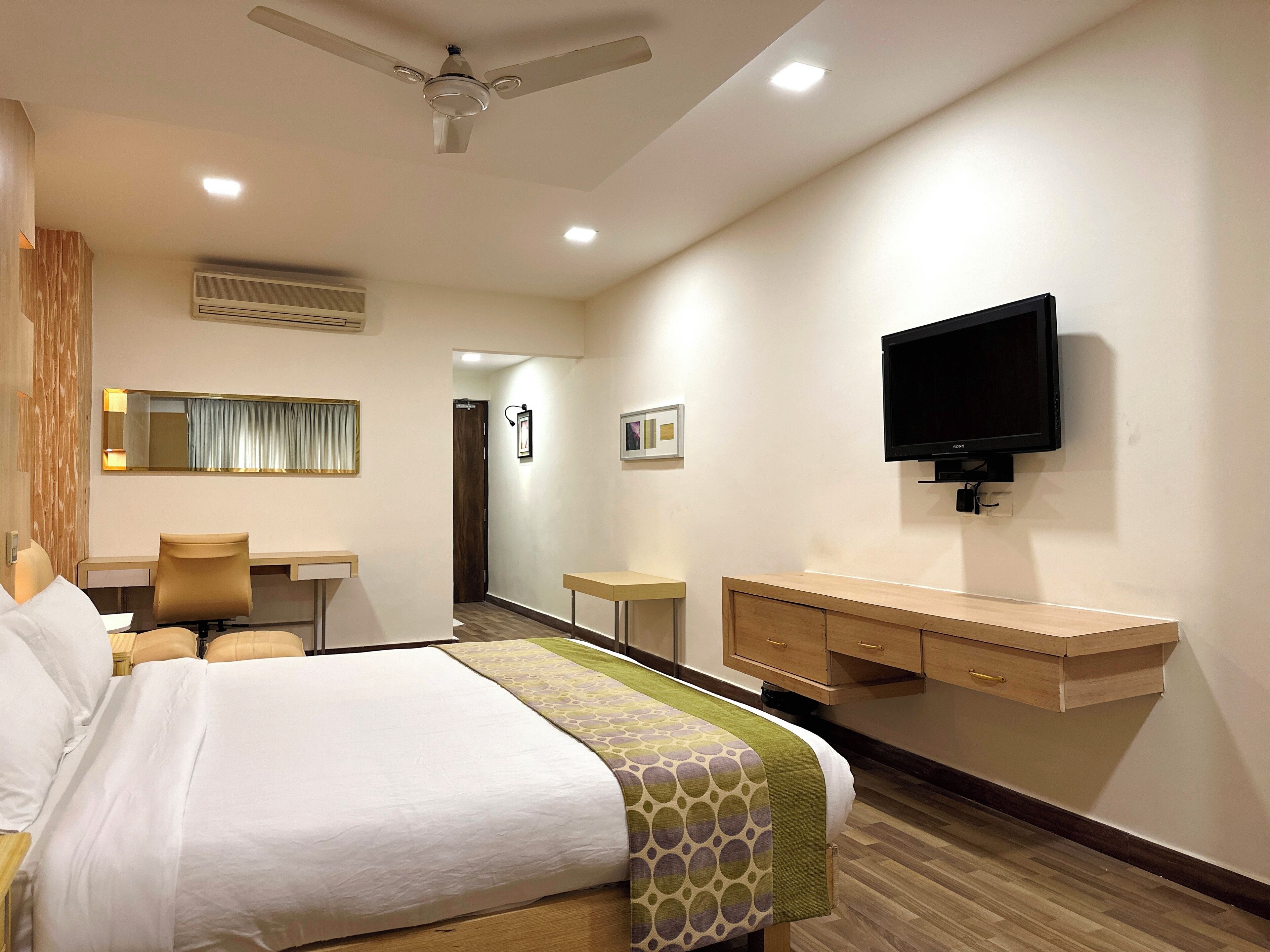 A hotel room with a bed, desk, chair, TV, and a wardrobe.