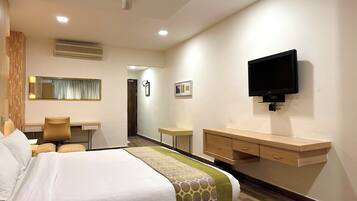 A hotel room with a bed, desk, chair, TV, and a wardrobe.
