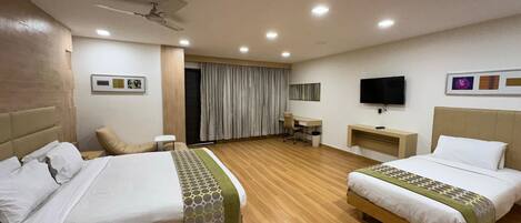 A hotel room with two beds, a desk, a chair, a television, and a ceiling fan.