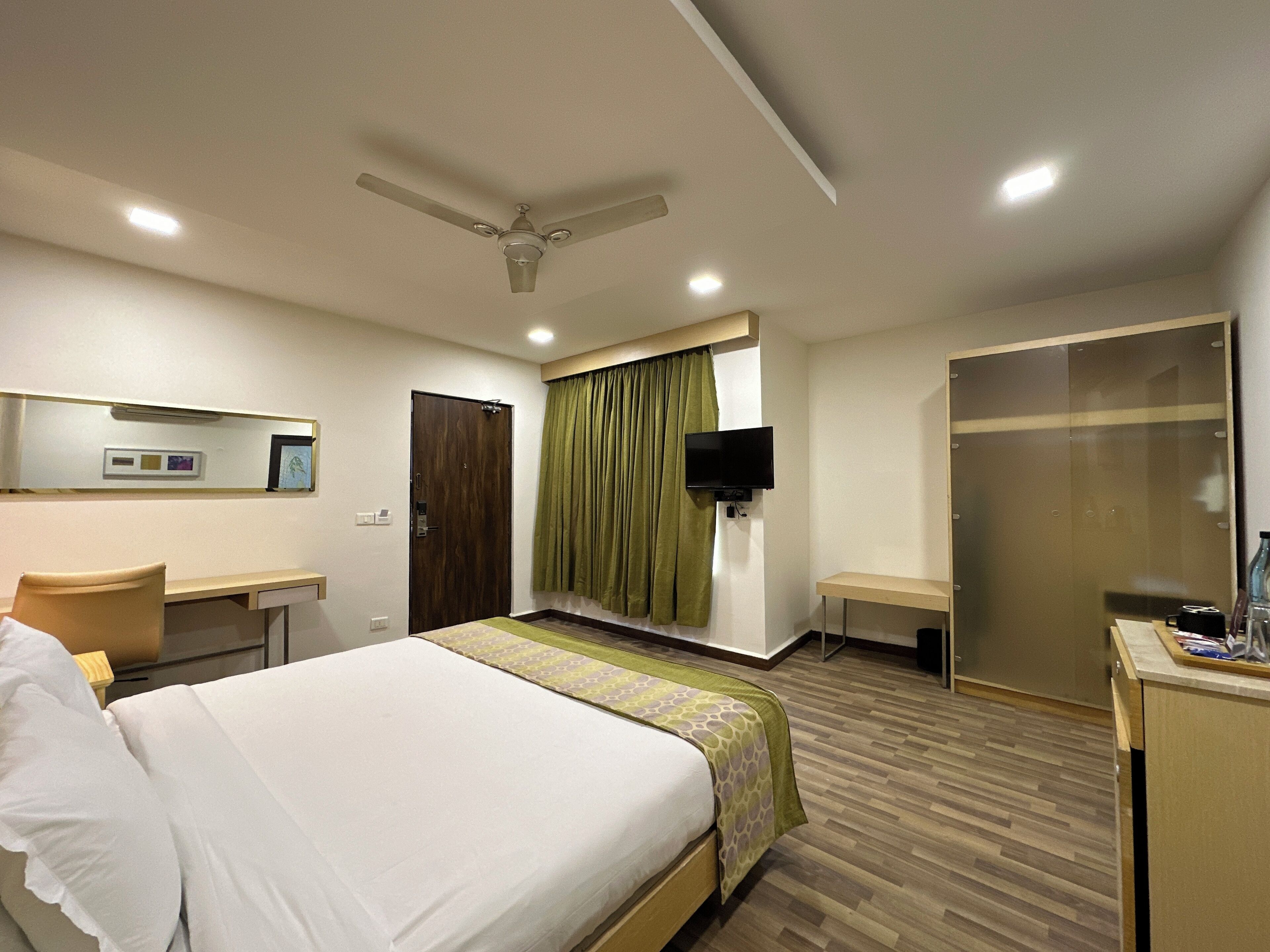 A hotel room with a bed, a desk, a television, a wardrobe, and a ceiling fan.