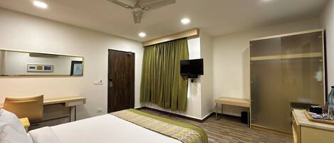 A hotel room with a bed, a desk, a television, a wardrobe, and a ceiling fan.