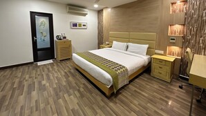 Un dormitorio moderno con una cama grande, suelo de madera, ventilador de techo, unidad de aire acondicionado, mesitas de noche y un tablero auxiliar.