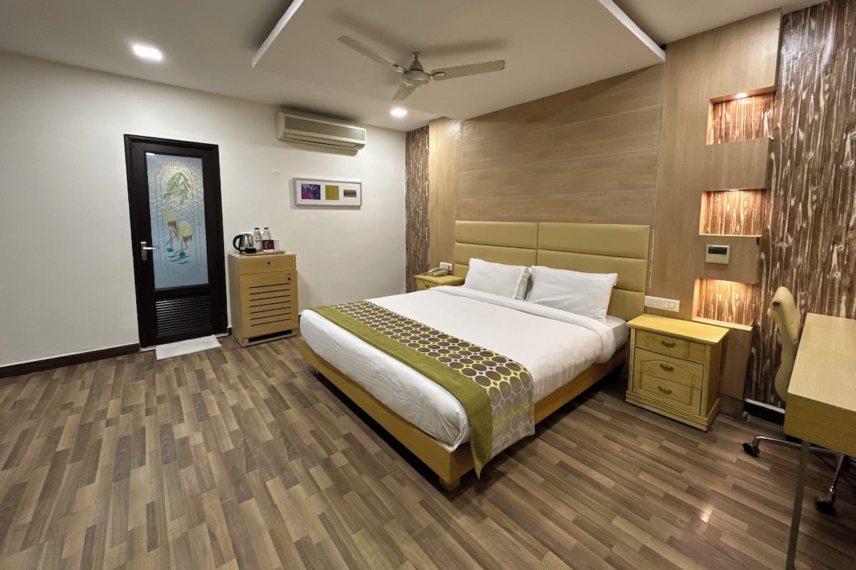 Une chambre moderne avec un grand lit, un plancher en bois, un ventilateur de plafond, un appareil de climatisation, des tables de chevet et une commode.