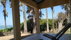 A covered outdoor area with a tiled floor, palm trees, and a view of the sea. - Unspoiled South Gambian Paradise '' Luxury Beach House '' (Kartung)