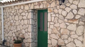 Un bâtiment en pierre avec une porte verte, un pot de fleurs contenant des fleurs rouges et un luminaire fixé au mur.