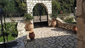 Une cour en pierre avec une arche centrale, des plantes en pot et un sol pavé.